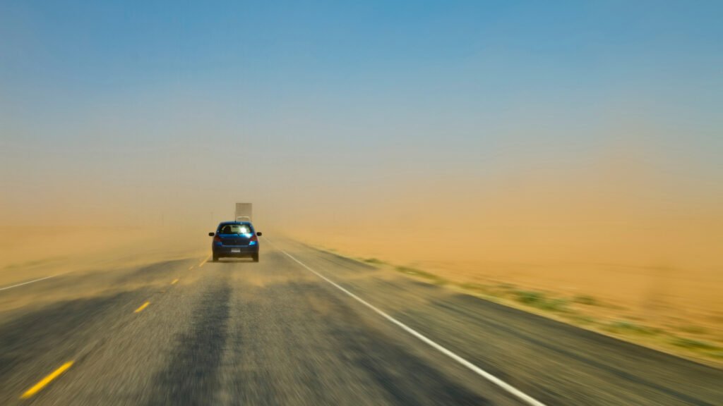Un automóvil avanza en medio de una tormenta de polvo con viento y visibilidad limitada.
