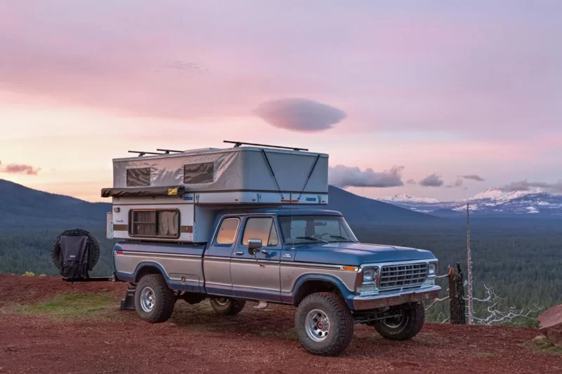 Una caravana de cuatro ruedas en un camión contra una puesta de sol y montañas.