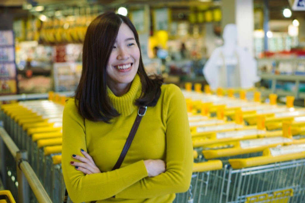 Una mujer asiática que sonríe en la tienda del carro de la compra.
