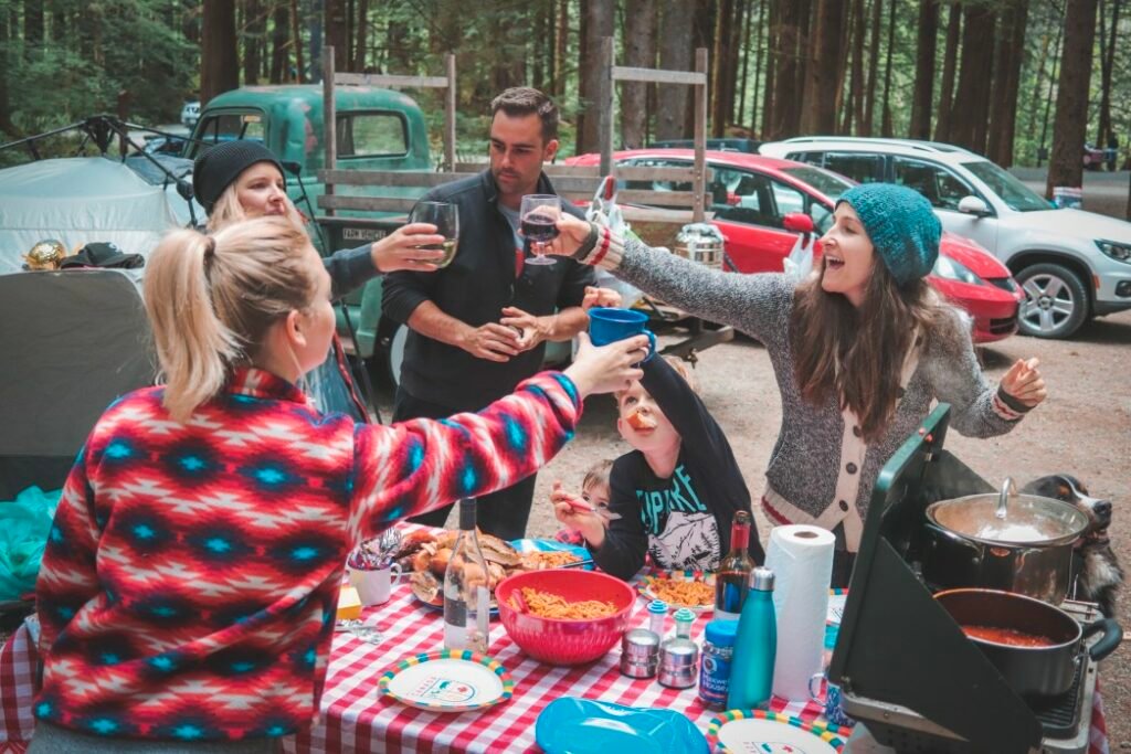 Una comunidad de campistas disfruta de una cena grupal en una mesa de picnic y brinda.