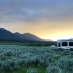 Una caravana grande está lista en un campo abierto con la puesta de sol detrás de las montañas.