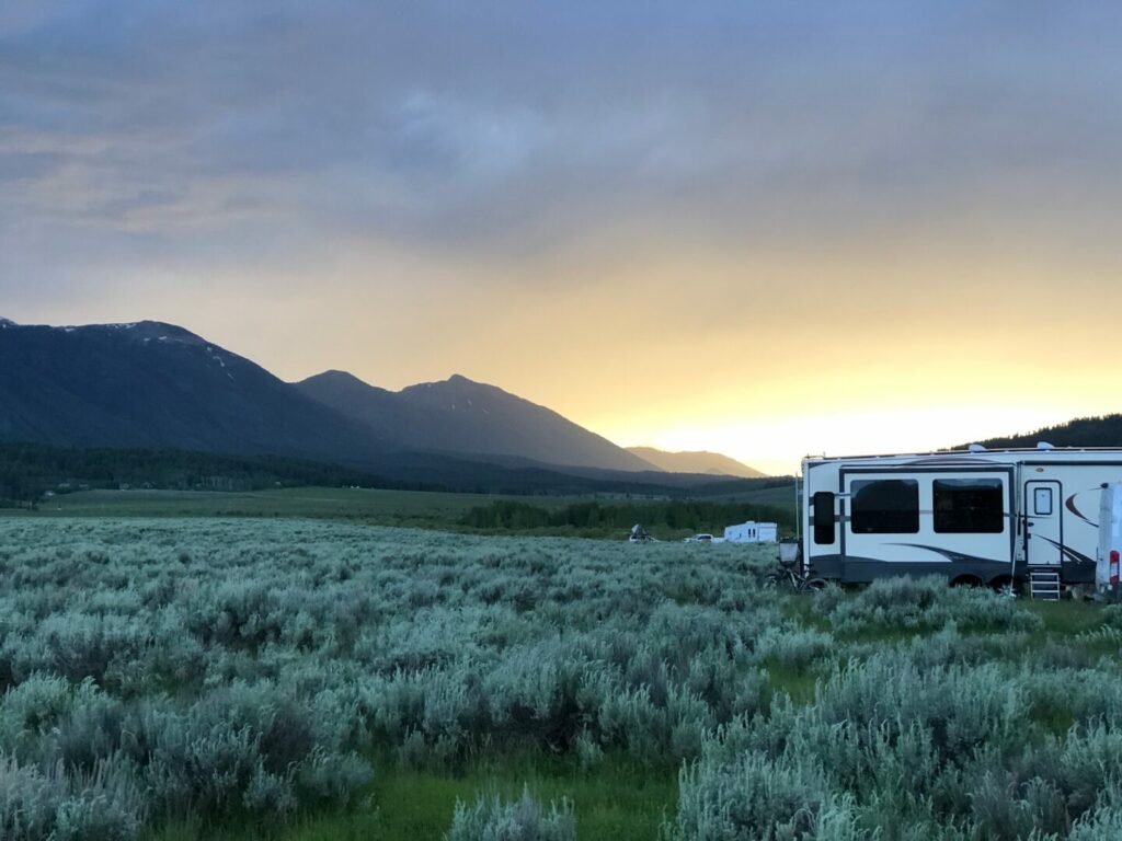 Una caravana grande está lista en un campo abierto con la puesta de sol detrás de las montañas.