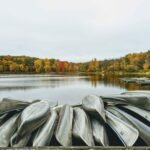 Hojas coloridas rodean un lago tranquilo a medida que cambian las estaciones en Indiana.  Las canoas retiradas durante el año yacían apiladas en primer plano.