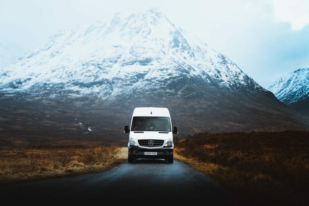Un RV Clase B conduce en invierno por una carretera remota con una montaña nevada detrás, donde amenaza una helada nocturna.