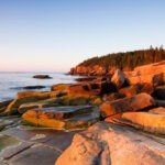La costa del Parque Nacional Acadia en Maine brilla con la luz rosada del atardecer.