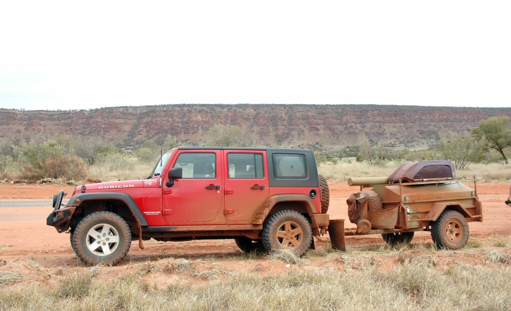 Un jeep rojo tirando de un pequeño remolque para ir de campamento