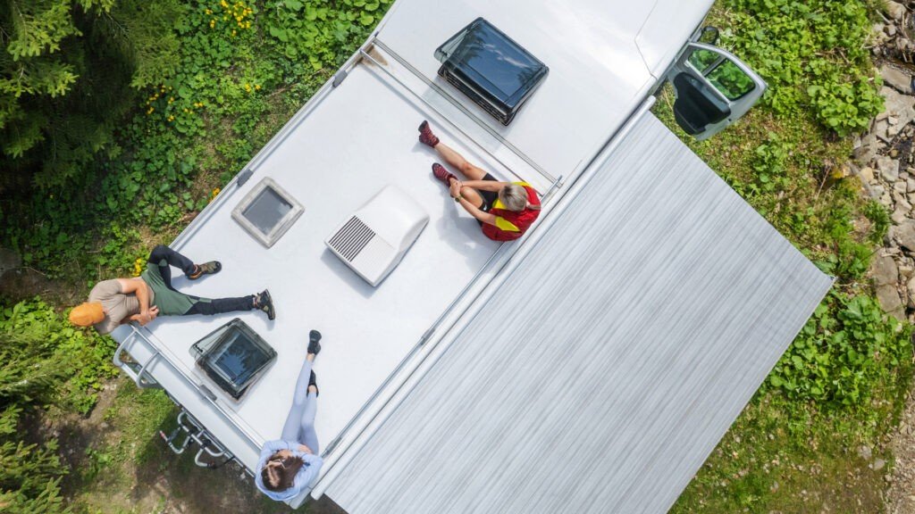 Un grupo de amigos se sientan en el techo de su RV después de aplicar un revestimiento de goma en el techo