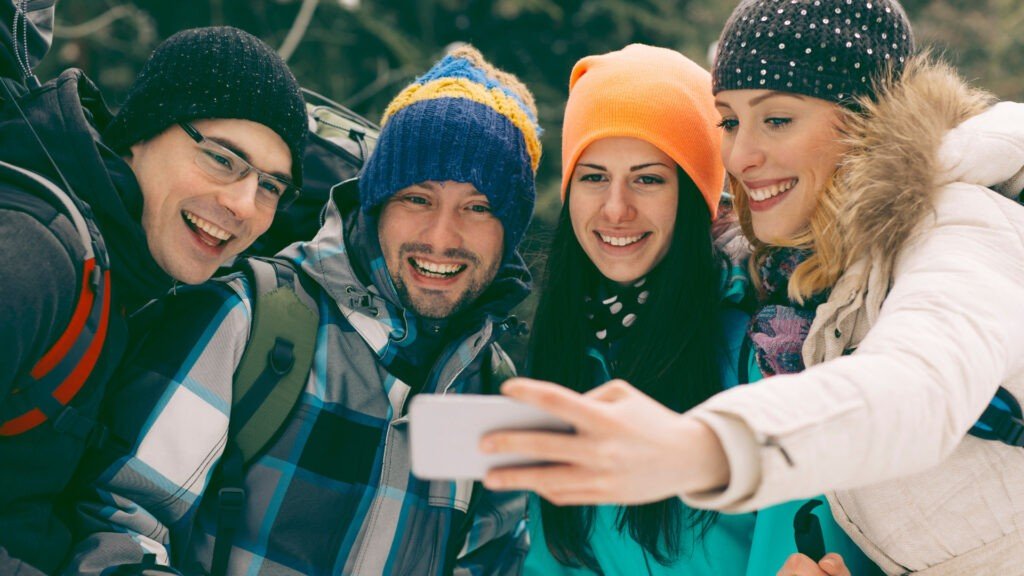 Un grupo de amigos tomándose una selfie mientras acampan en invierno, vestidos en capas después de seguir estos consejos para acampar